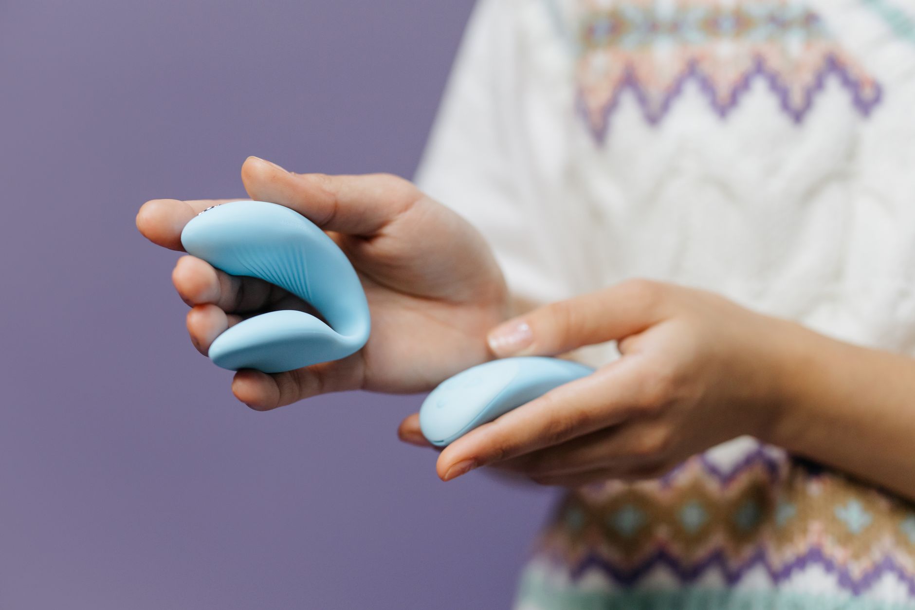 Close-up of hands holding a sleek lemon vibrator against a purple background, symbolizing intimacy and shared exploration.