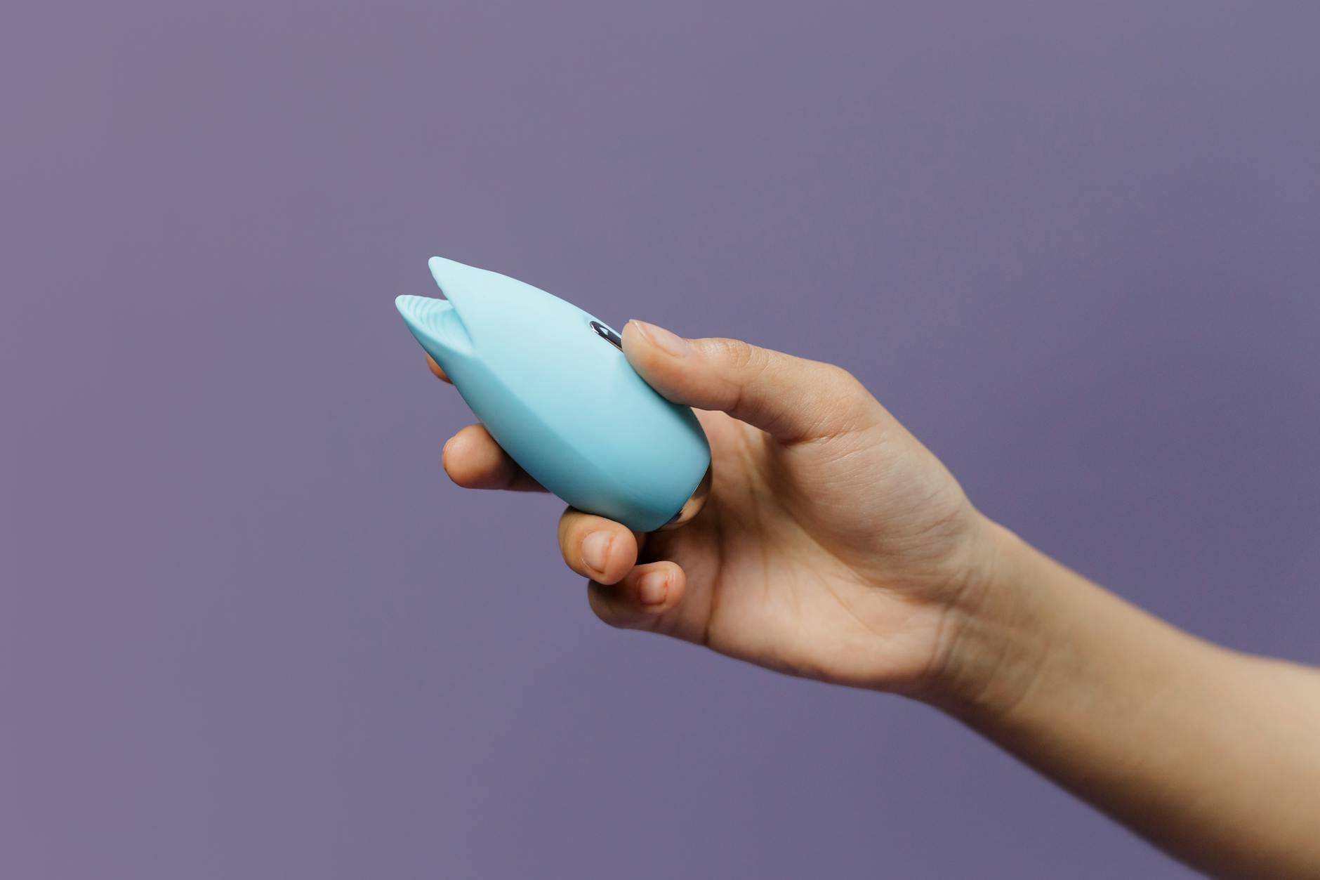 Blue silicone vibrator held in hand against a purple background
