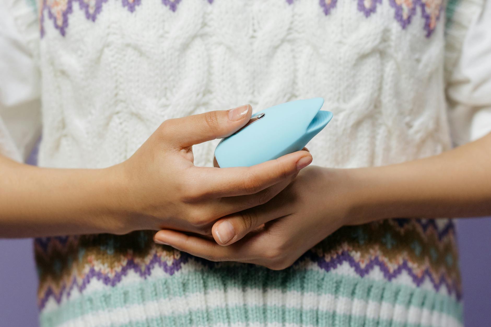 Uma mão segurando um vibrador azul contra um suéter texturizado.