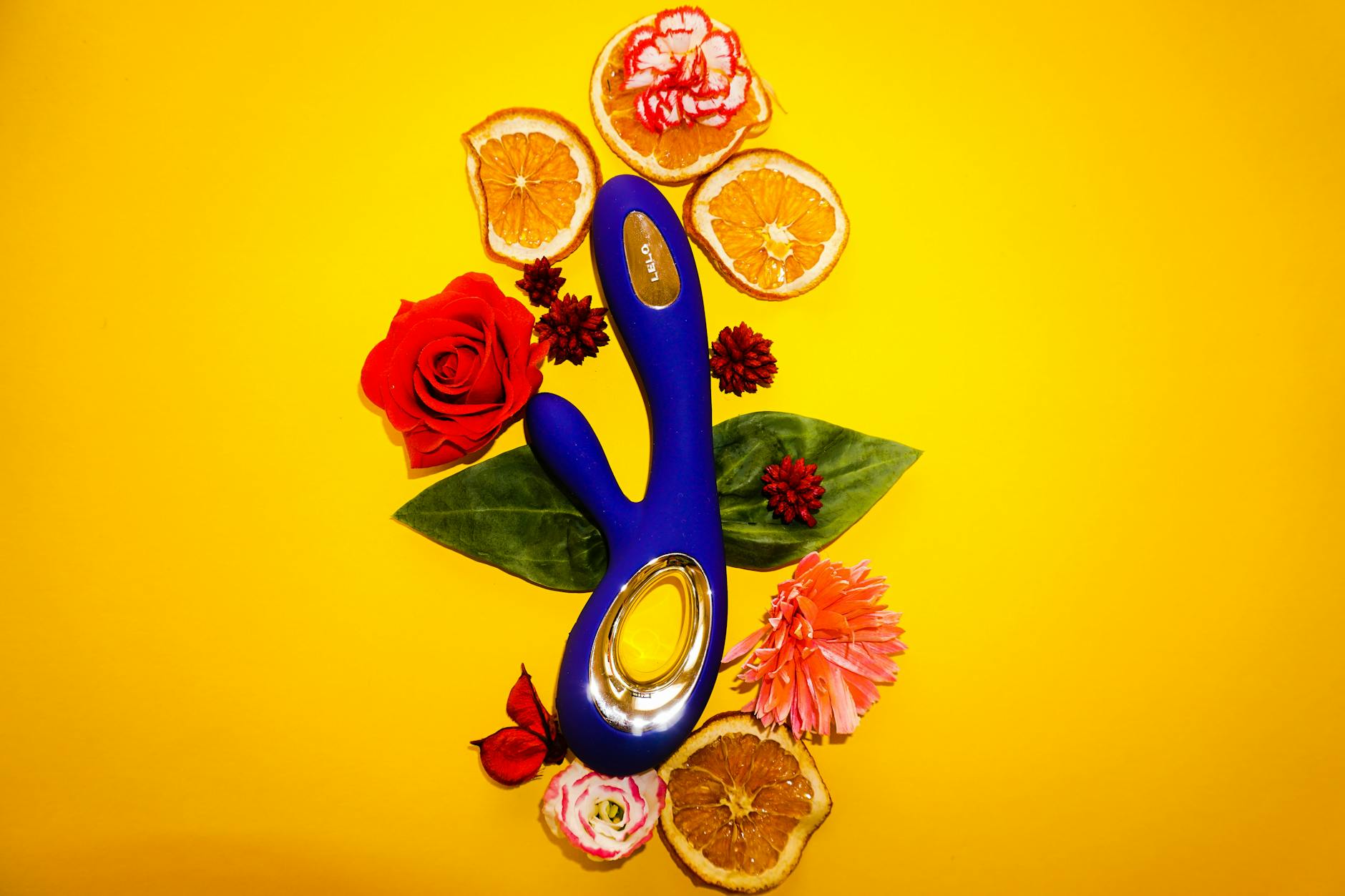 Blue clitoral vibrator surrounded by fresh lemons and citrus fruit on yellow background