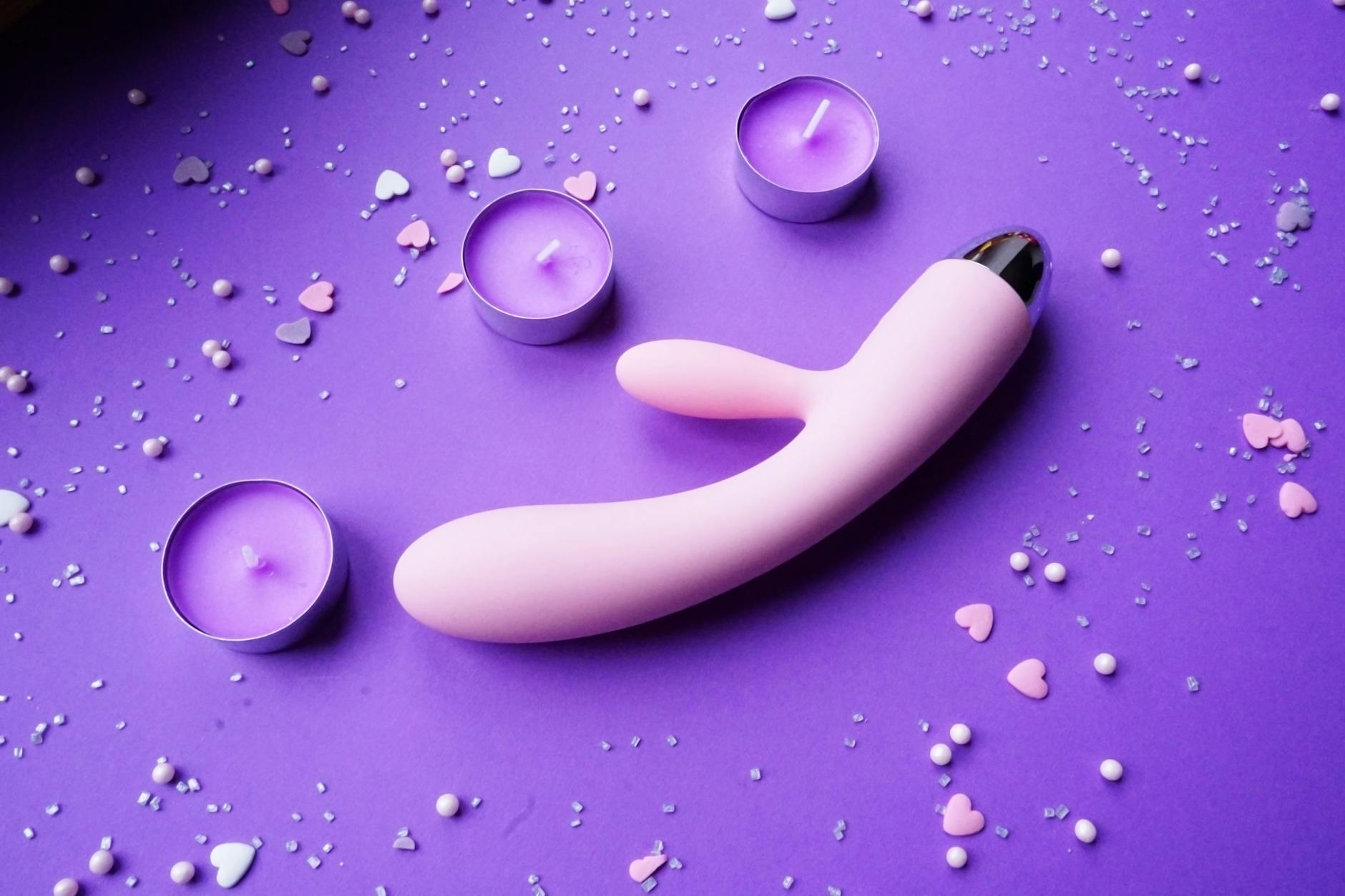 Vibrador de silicone azul sendo segurado contra fundo roxo sólido, promovendo amor próprio e sensualidade